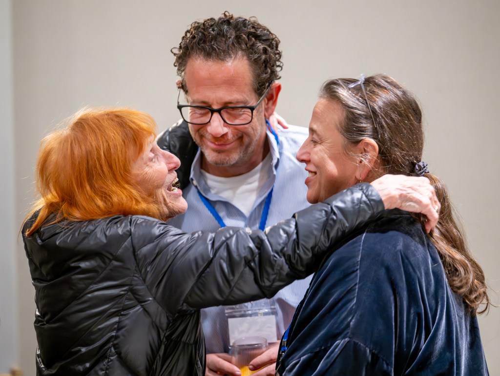 Three individuals engaged in a warm conversation, showcasing smiles and camaraderie at a community event.