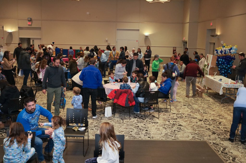 A bustling indoor event space with families and children engaged in activities, seated at tables decorated with festive themes.